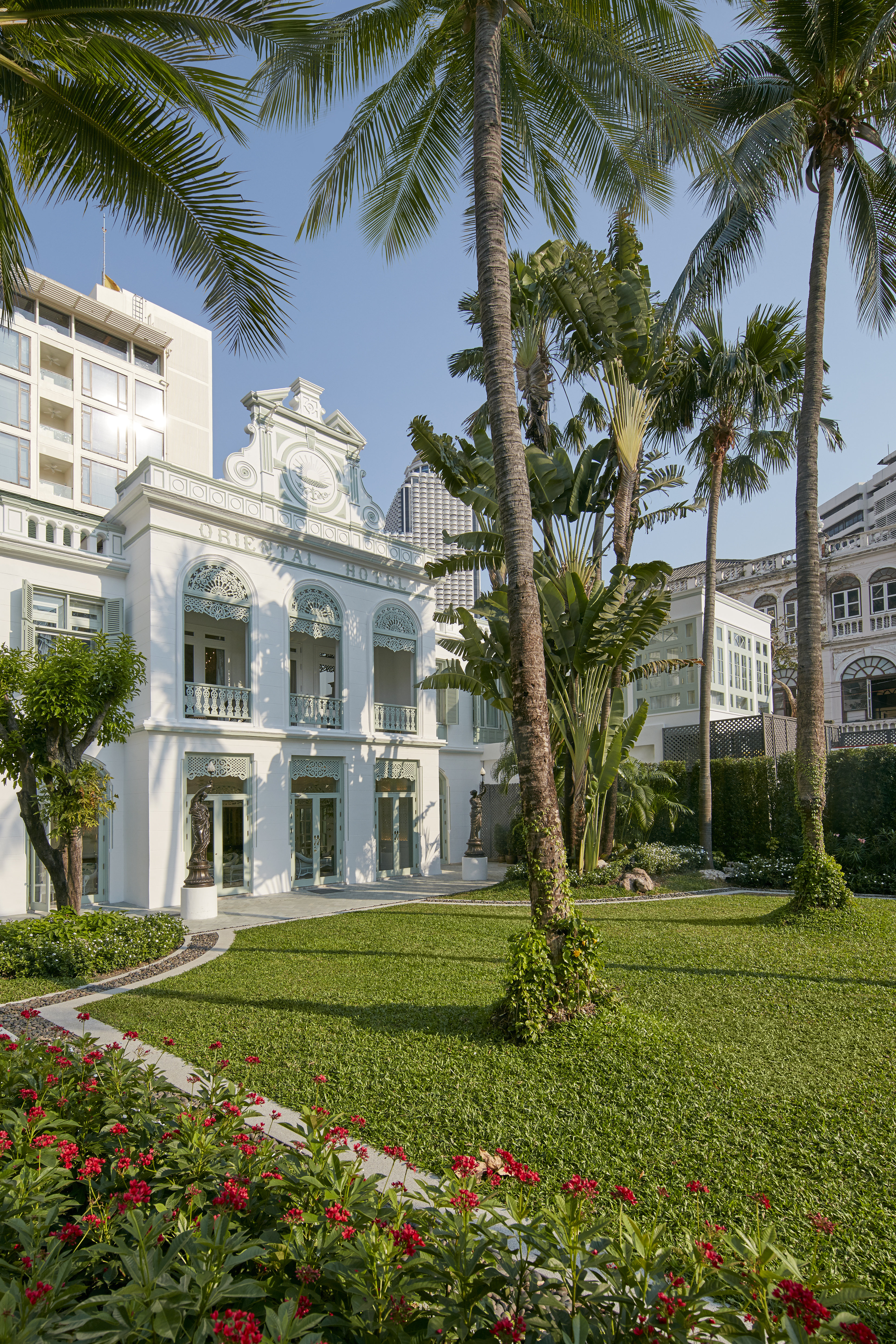 Mandarin Oriental Bangkok riverfront garden showing the hotel's pool area framed by tropical palms with the Chao Phraya River beyond