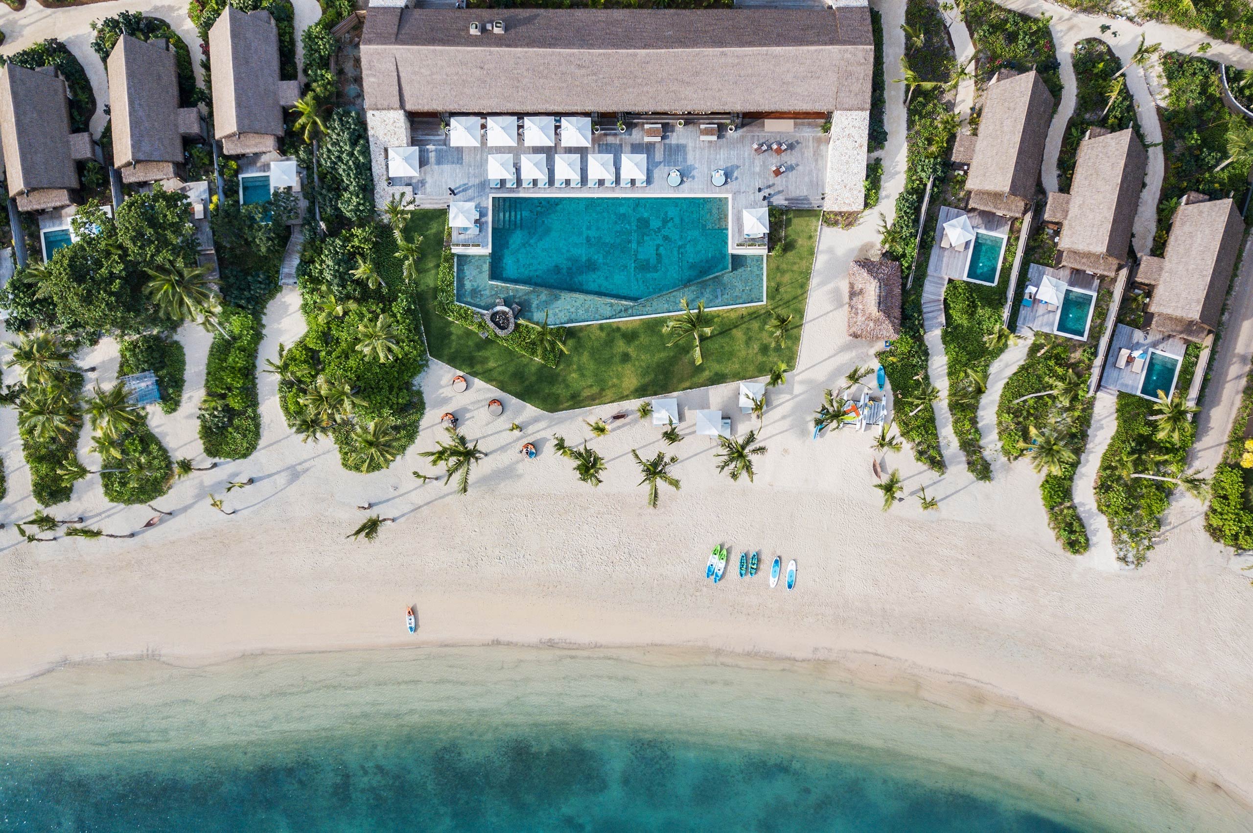 Aerial view of Six Senses Fiji on Malolo Island with the substantial thatched main pavilion, the dedicated central pool, and the private-pool villas along the white-sand Malolo lagoon beachfront