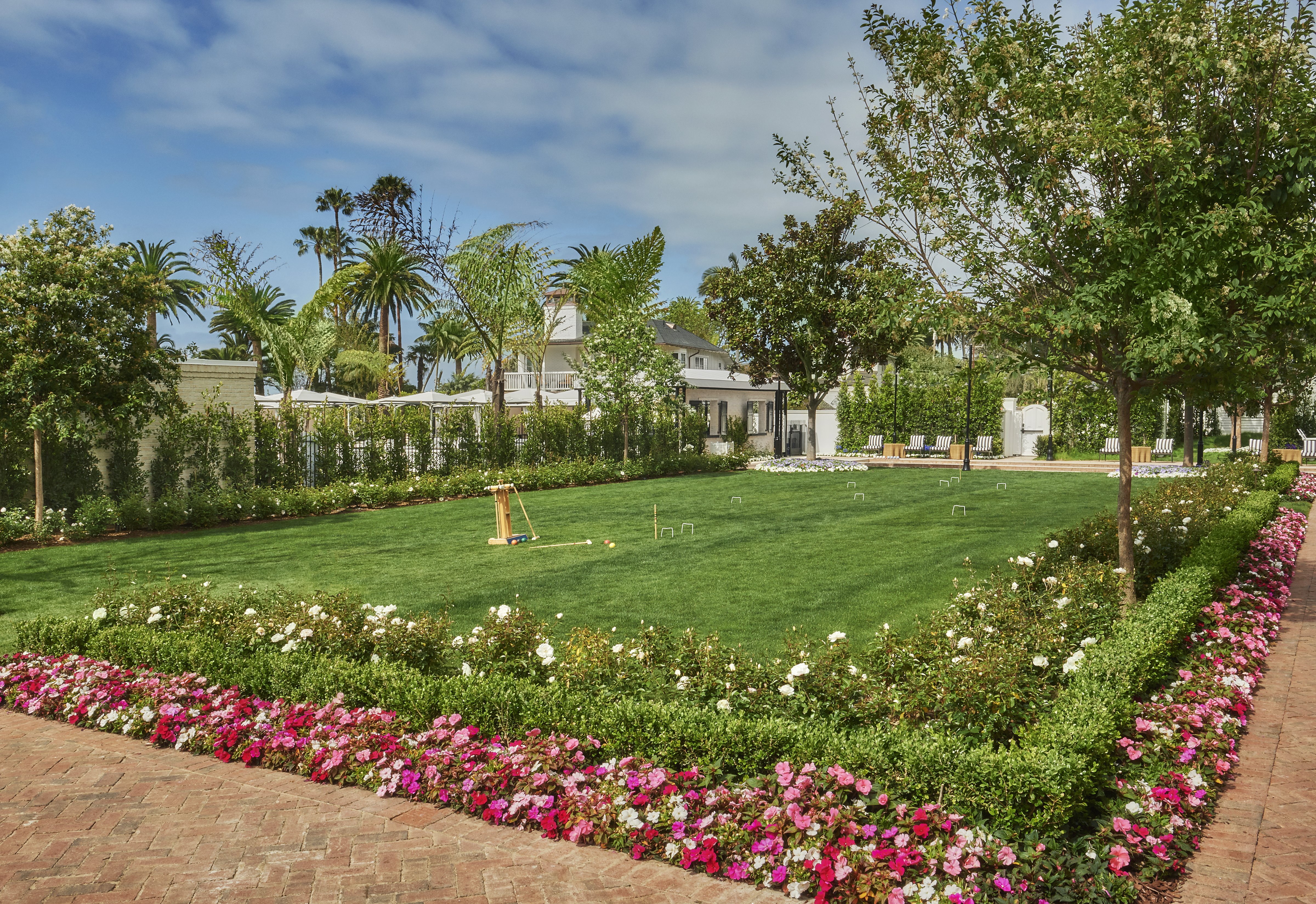 The croquet lawn at Rosewood Miramar Beach bordered by roses and impatiens with cabanas beyond - the kind of estate grounds that reward a multi-night resort stay where the property itself is the destination