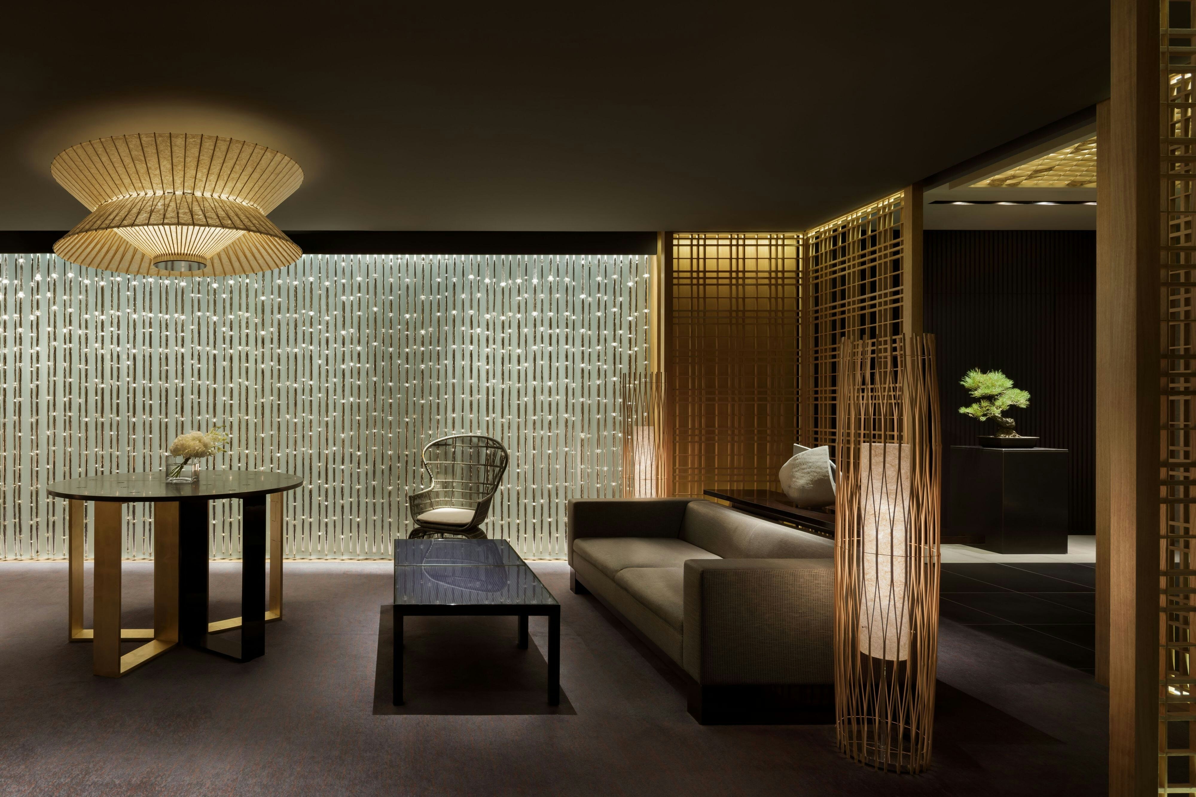 A lounge at The Ritz-Carlton, Kyoto with kimono-textile-inspired screens, a woven washi pendant light, bamboo floor lanterns and a bonsai on a plinth - the commissioned craft and material depth that separates a 5-star interior from a well-decorated 4-star one