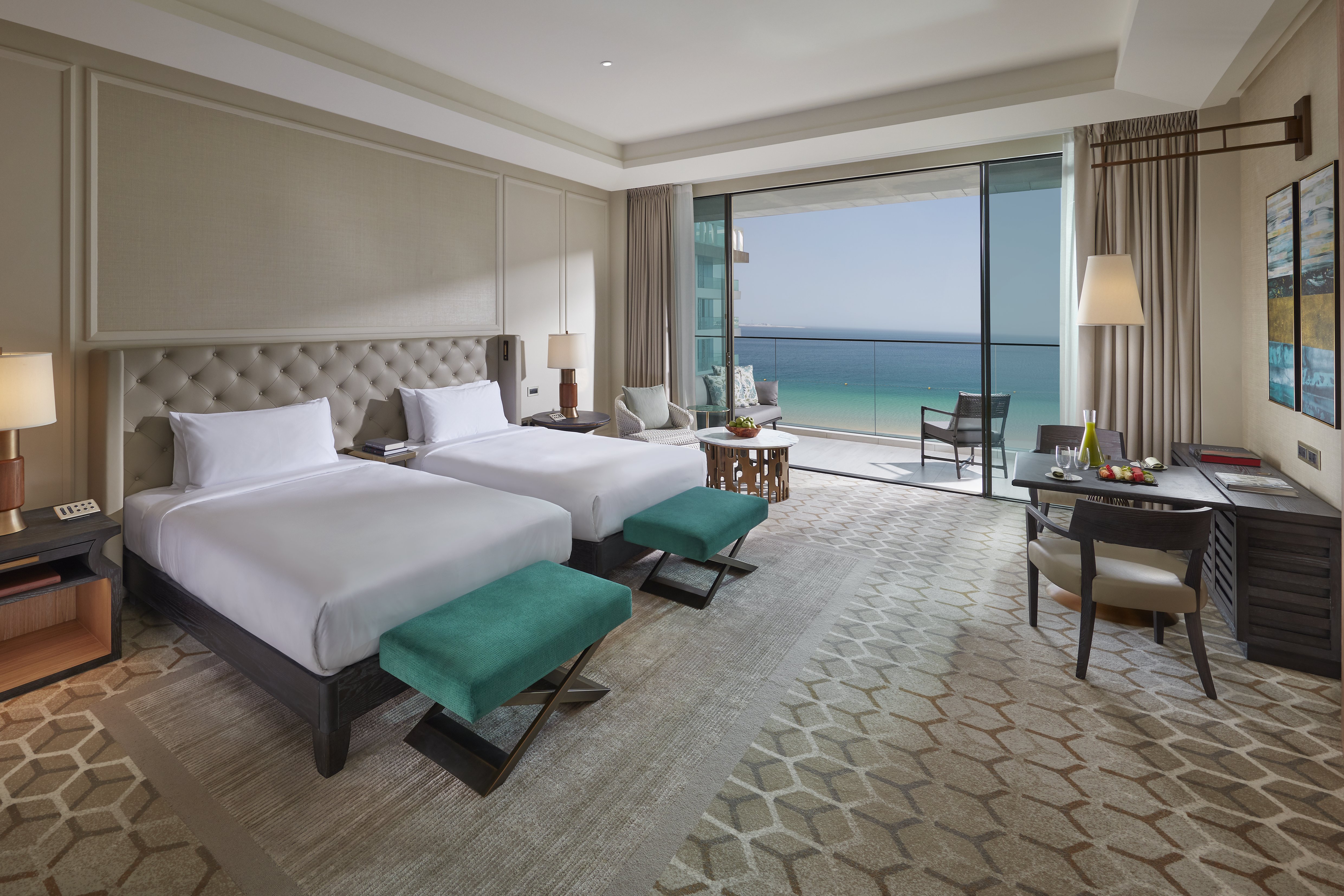 A sea-view guest room at Mandarin Oriental Jumeira, Dubai with twin beds in white linens, a writing desk with a welcome fruit plate, a seating area and a private balcony over the Arabian Gulf - the standard inclusions of a 5-star hotel room