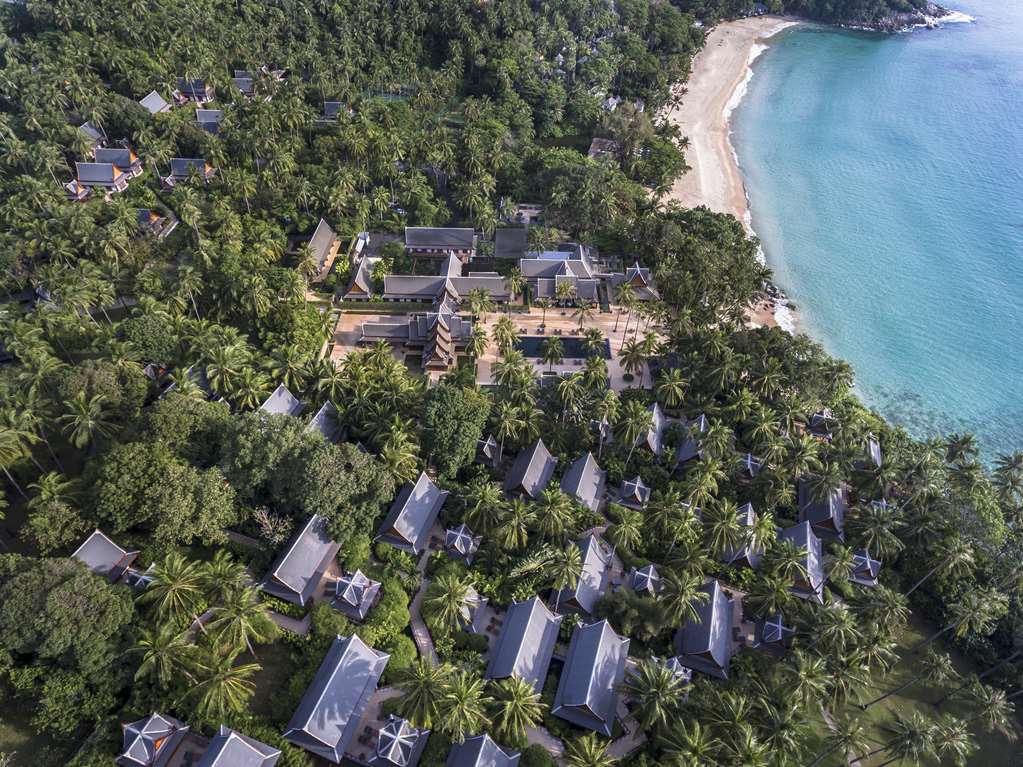 Aerial view of Amanpuri in Phuket showing the central pavilions and pool with pitched-roof villas scattered through the coconut grove above Pansea Beach - a property built around staffing ratios of several employees per guest