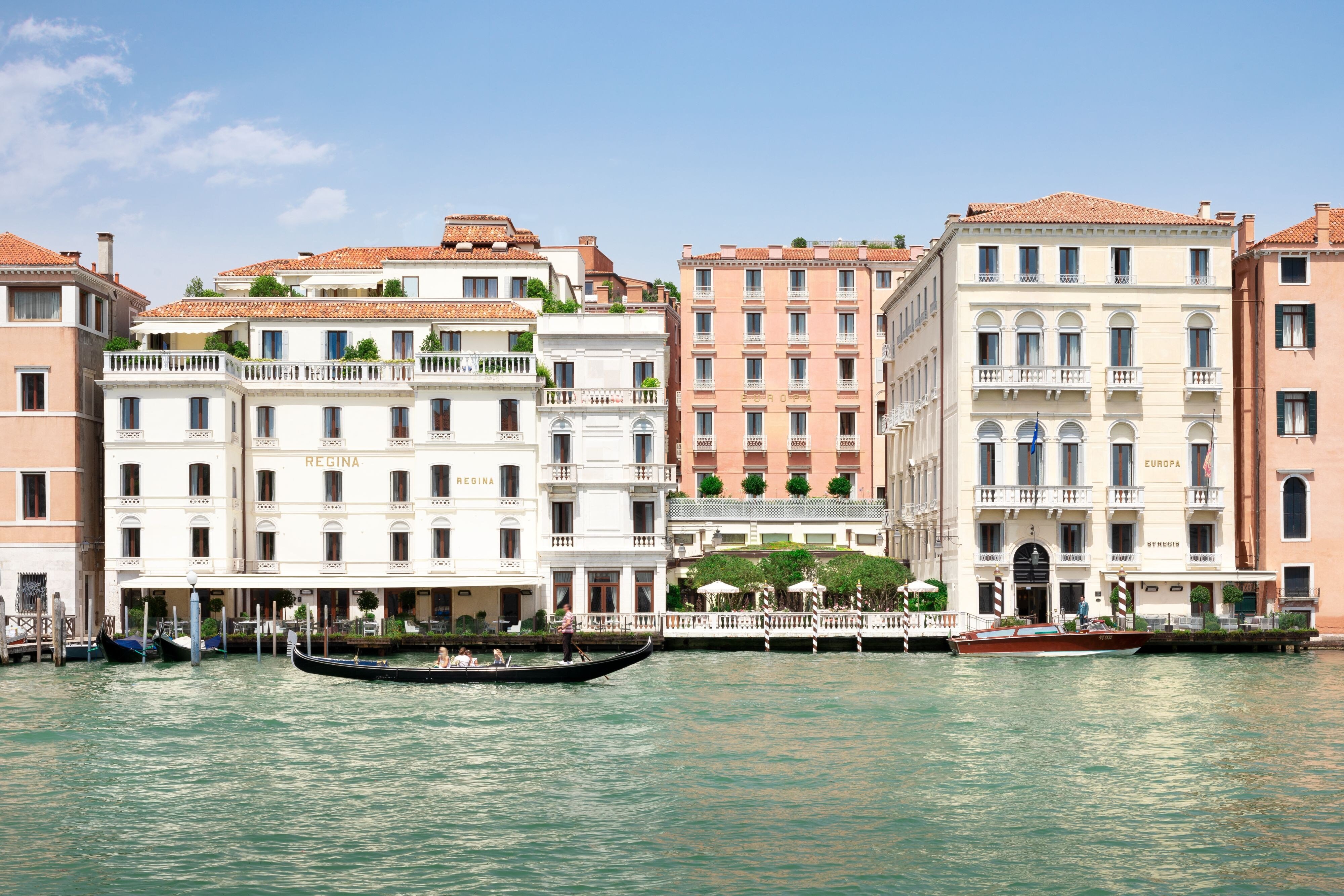 The Grand Canal facade of The St. Regis Venice with its Regina and Europa palazzi, canal-side terraces, and a gondola passing - a property whose rates swing dramatically between Carnival-to-October peak and the November-to-February low season